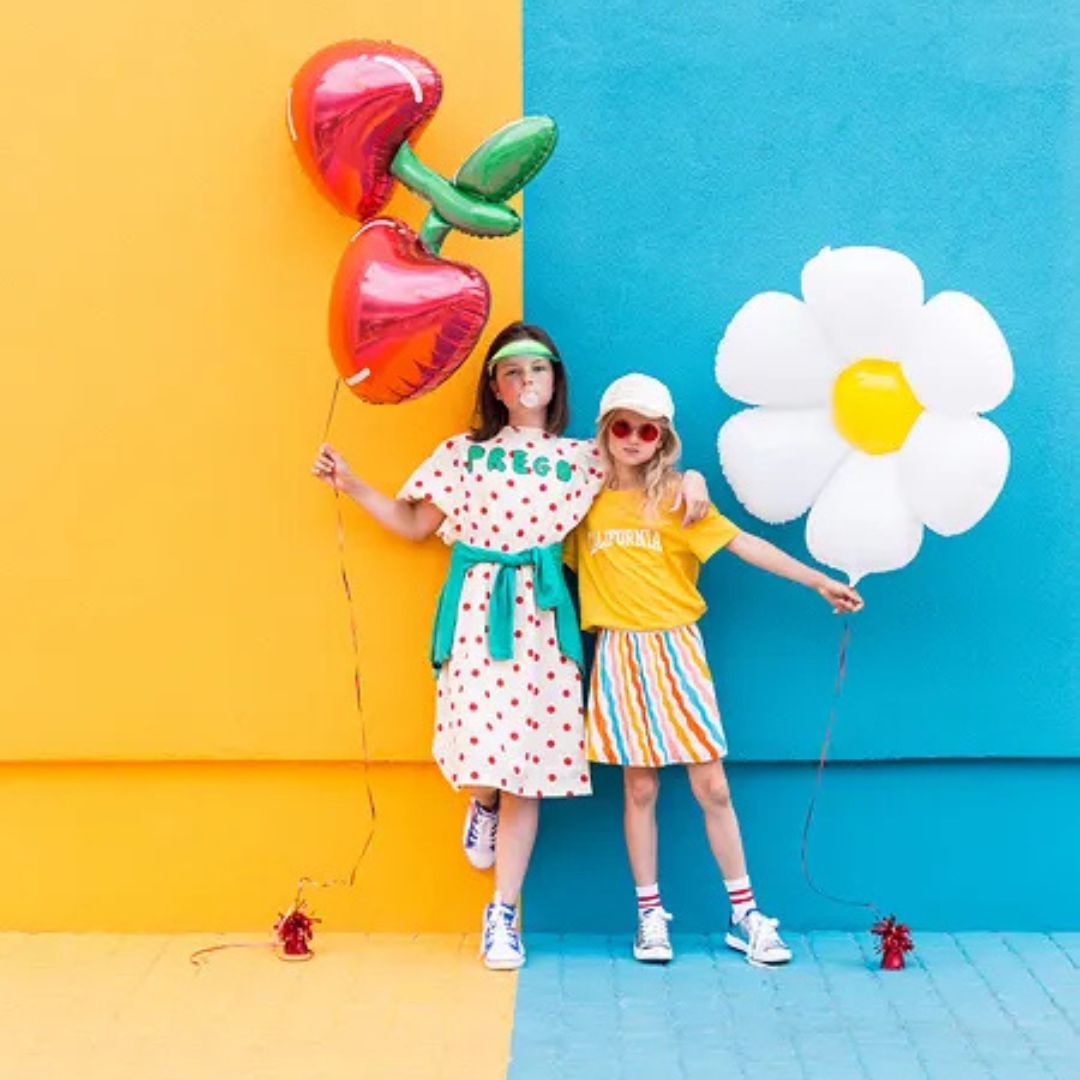 dos niñas con globos con helio de forma de cereza y flor margarita