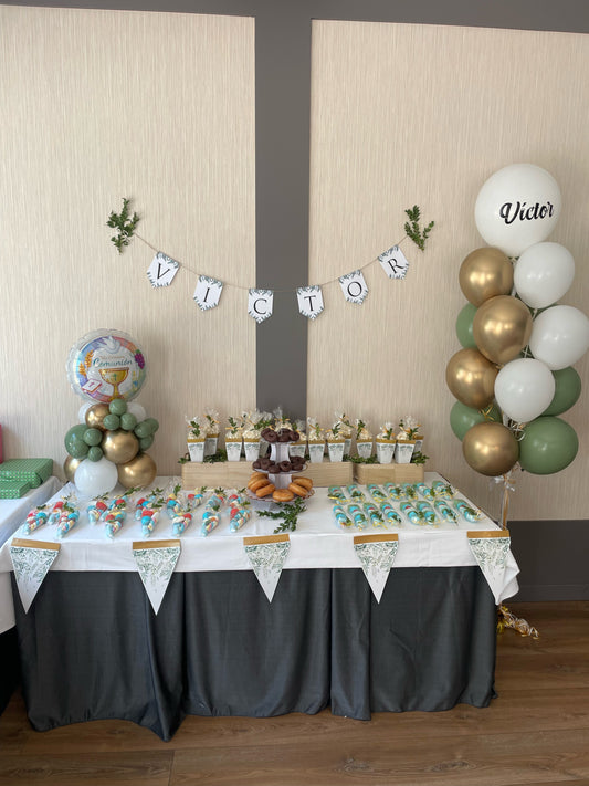 Mesa decorada para celebrar un cumpleaños con todos dorados, blancos y verde pastel. Además incluye un boquete de globos personalizados con el nombre de victor en el globo principal y un ramillete de globos de colores combinados al rededor.